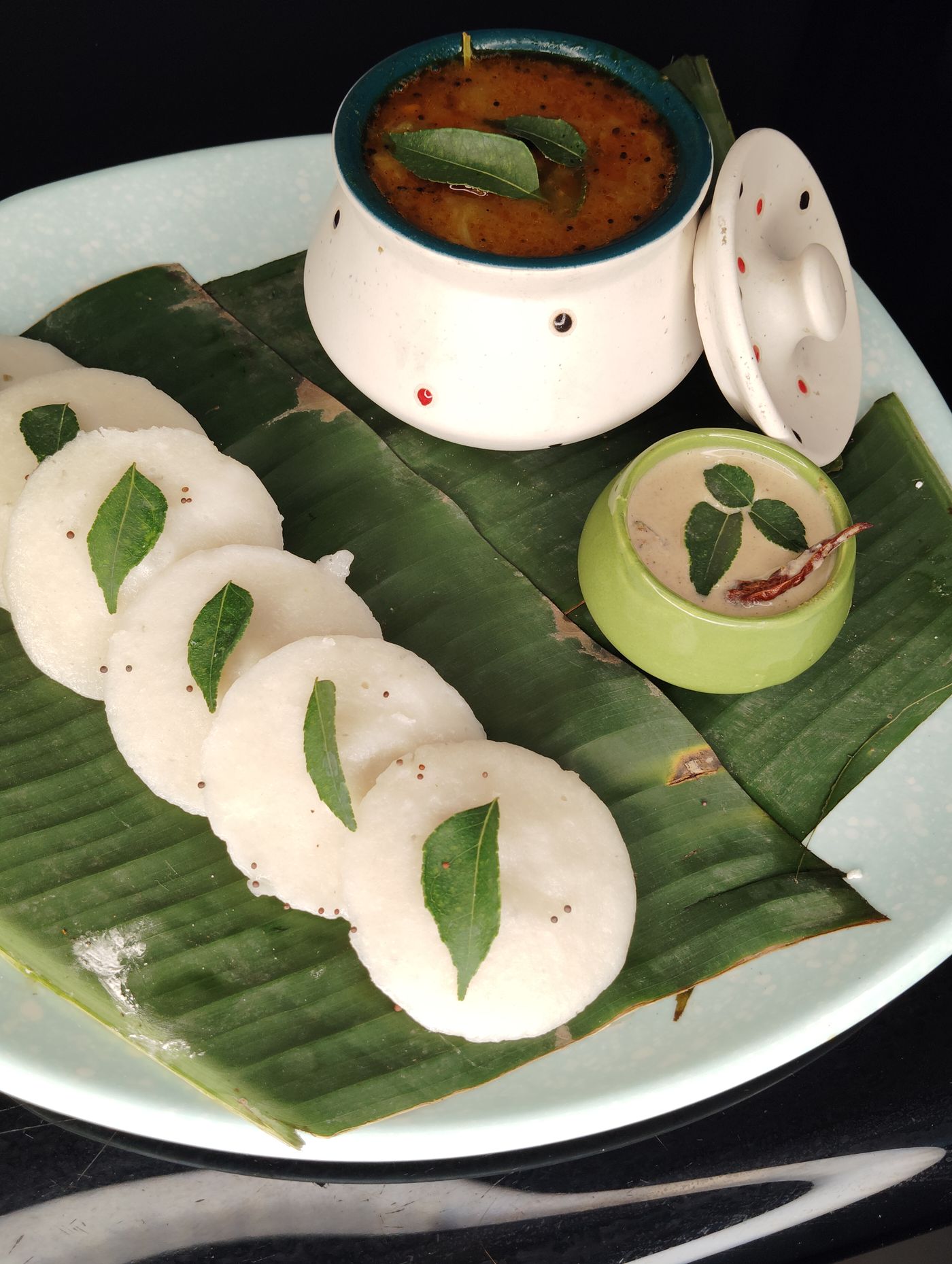 Idli served on a banana leaf with chutney.